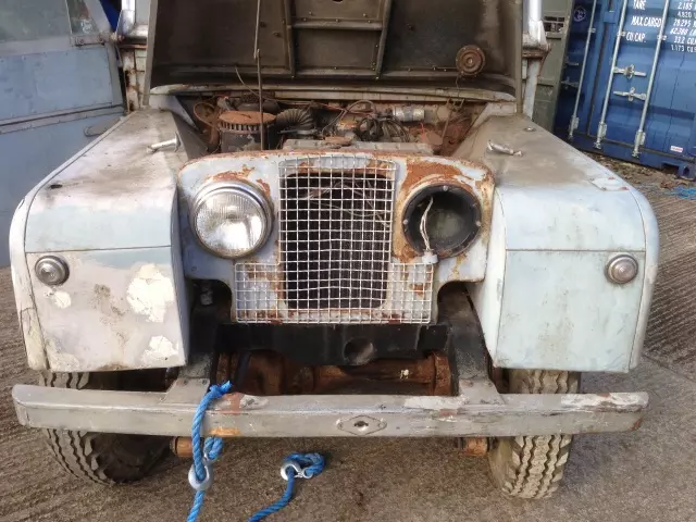 An old rusty land rover parked in a warehouse.